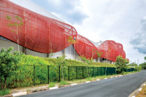 The west facade of the Brazilian Paralympics Centre in São Paulo is shielded by large undulating shapes made of coated polyester mesh (colored a golden red to evoke Olympic medals) that reduce heat buildup and allow the space to function without mechanical air conditioning. Fabrics used are Soltis FT 381 (custom red mesh) and Précontraint 502 (white liner on upper façade) from Serge Ferrari. Photo: Serge Ferrari.