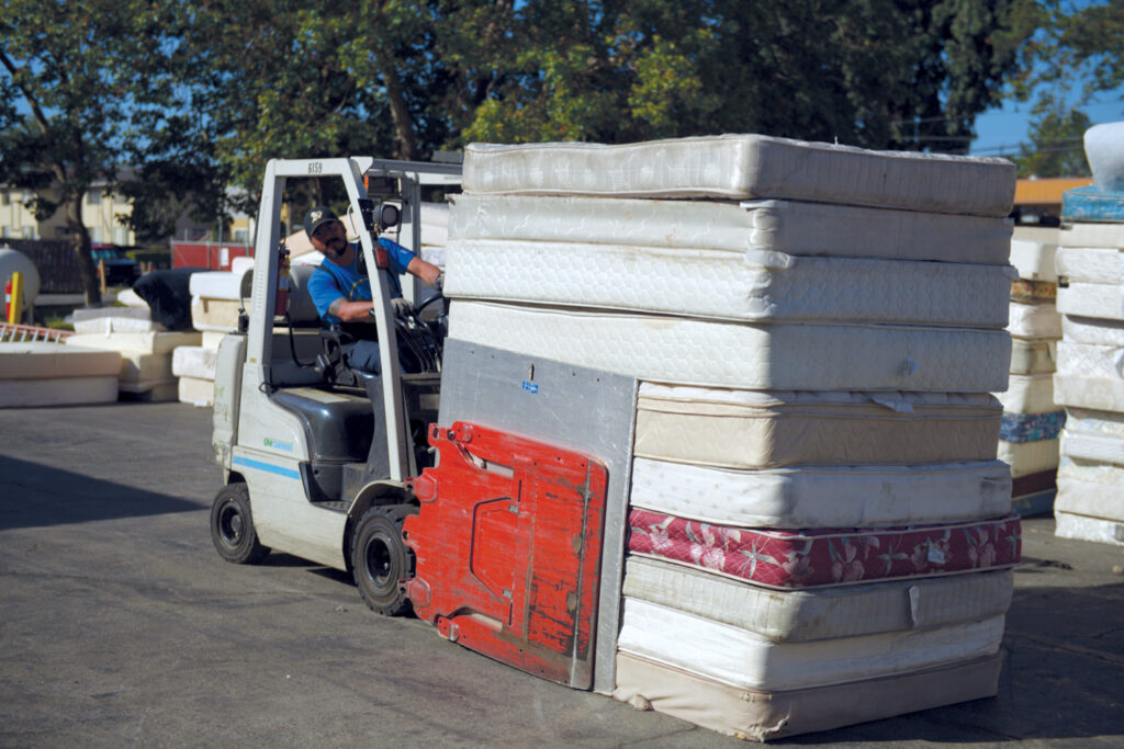 A man drives a forklift to move a stack of 10 mattresses. Research finds recycling mattresses can be a source of materials to make EV batteries.