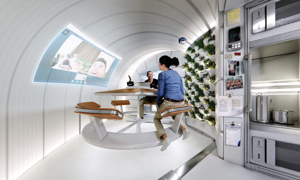 A concept image of the completed Orbital Reef from the inside, showing astronauts seated at a table, with a kitchenette and plants to the right and a screen projected on the wall at left.