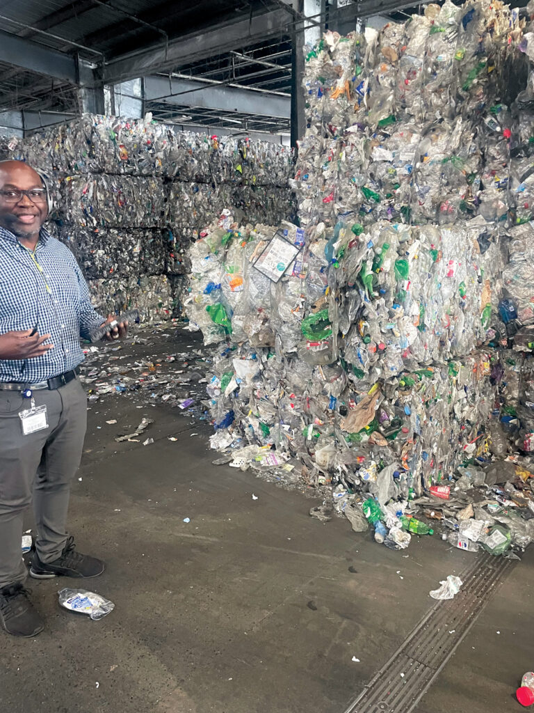 UNIFI plant manager Kerby Stone in front of stacks of bales of recycled bottles explaining the recycling process
