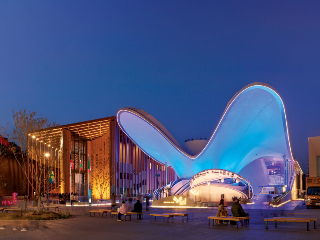 The State of Kuwait's pavilion at World Expo 2025 in Osaka, lit up at night in blue and lavender. It is made of curved tension fabric