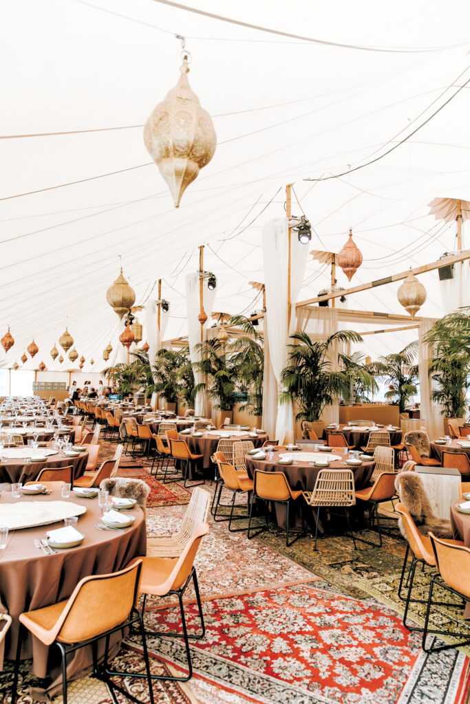 The inside of a tent featuring white tapestries hanging from he ceiling and tables and chairs.