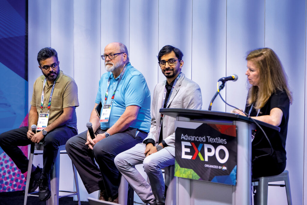 Panel discussions take place at Advanced Textiles Expo. This is the panel on artificial intelligence at the Anaheim event in 2024. There are three experts seated on stools and a moderator at far right asking questions while seated behind a podium. From left are Anirudh Sharma, Jim Joyce, Manu Venkataramu and Paige Mullis.