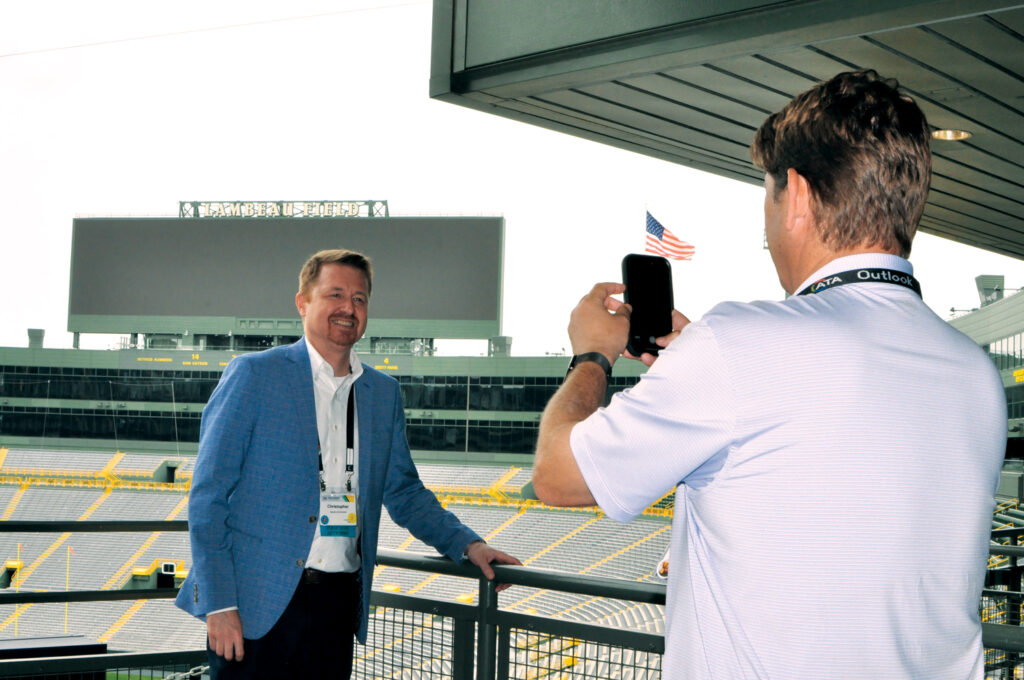 Outlook Leadership Conference attendee Chris Persson, being photographed by another attendee, with Lambeau Field in the background