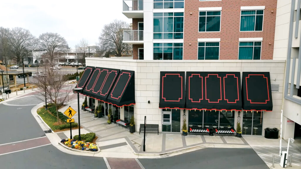 The tall awnings installed at Gourmand Market by Patriot Awning in Charlotte, N.C., have a powder-coated aluminum framework and are black Sunbrella® fabric with custom-cut Serge Ferrari red appliqués sewn onto the face and valance.