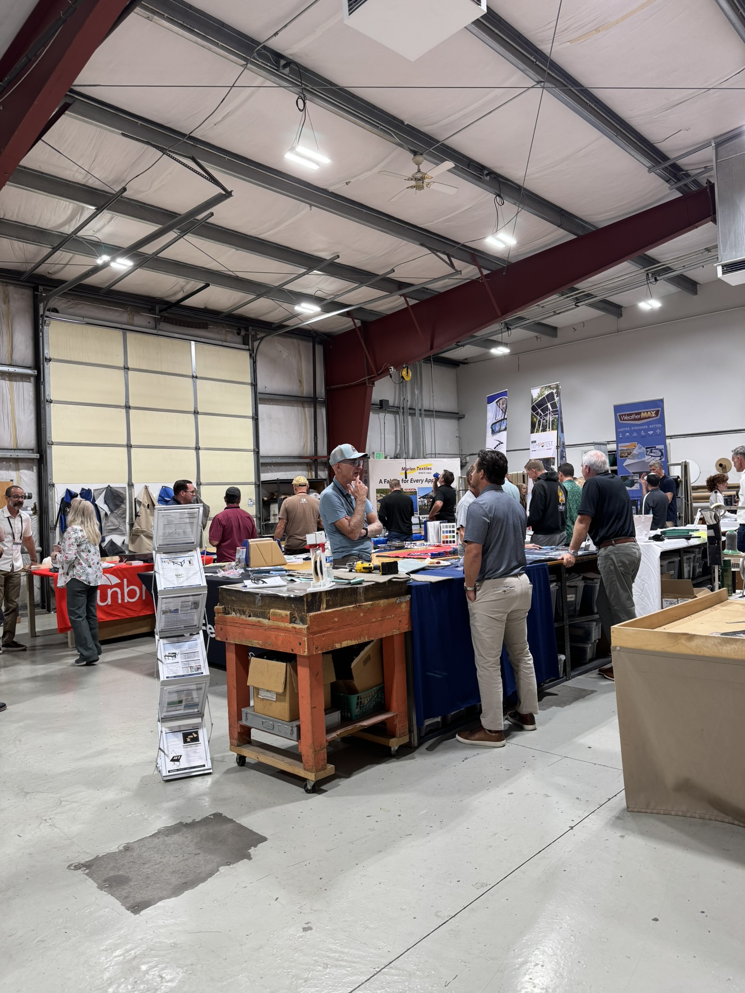 Fabricators chat with suppliers at many exhibitor tables in a shop.