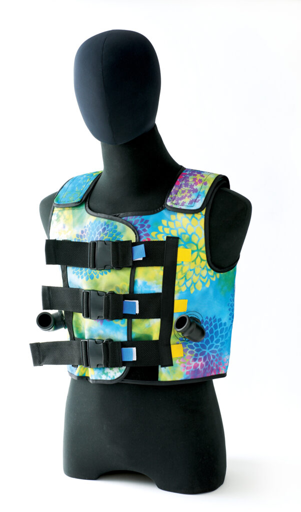 A cystic fibrosis vest on a black mannequin. Itis brightly colored with splashes of bright yellow, purple blue and green with mum flowers on it. In front it straps tightly with buckles and has two outlets for hoses to plug into.