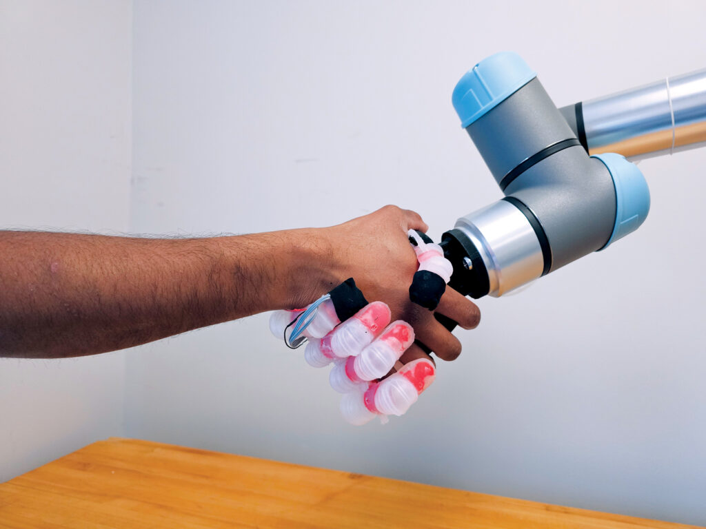 A human forearm and arm are shown shaking the hand of a robotic arm.
