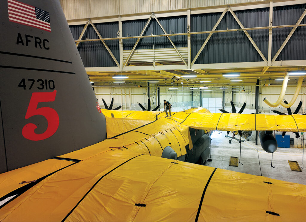 SkyShield yellow fabric shown on a C-130 aircraft to protect it from mail damage. The plane is in a hangar being worked on.