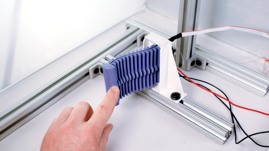 A hand presses on a soft purple structure in a white laboratory environment.
