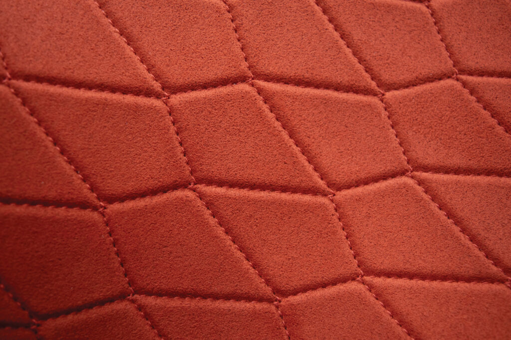 Close-up view of Shamut Corporation’s Neoluxe™ Onyx in the color Ember, which is a deep red-orange, showing the stitching pattern in horizontal flowing V-shapes