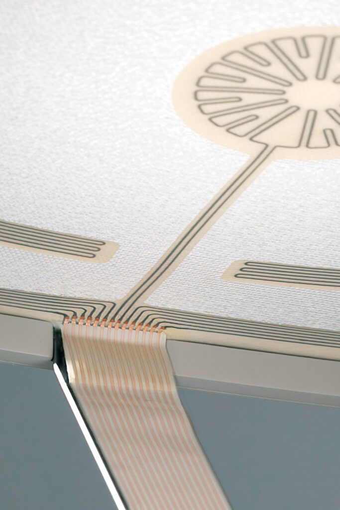 Close-up of the connections between the conductive paths  on the smart textile, which is white, and the control unit. 