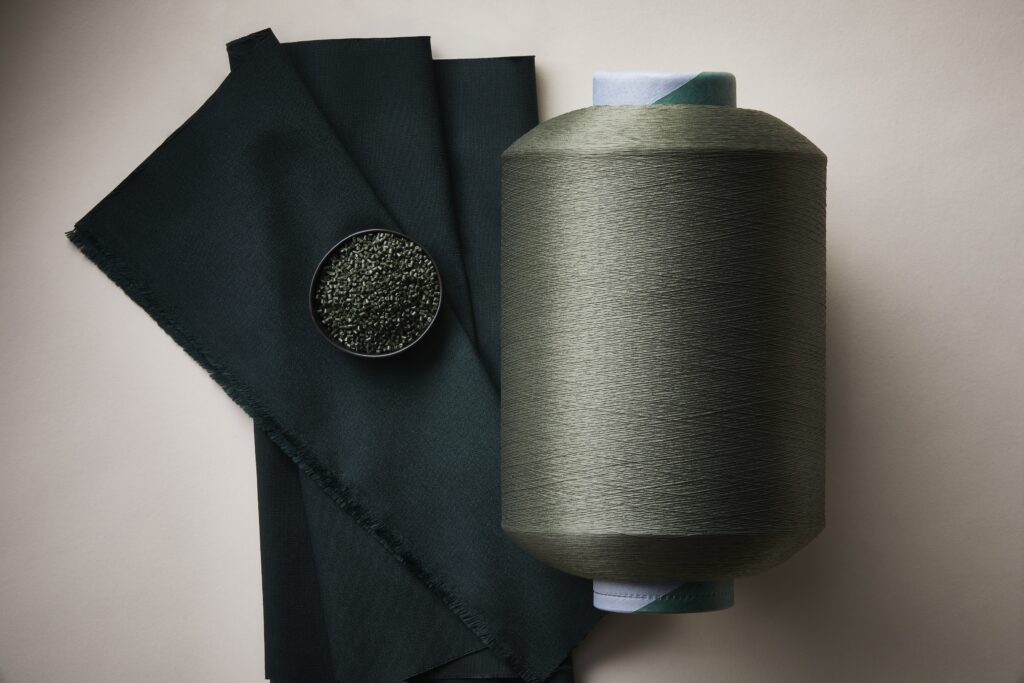 A fabric sample, cup of powdered dye and a spool of yarn.