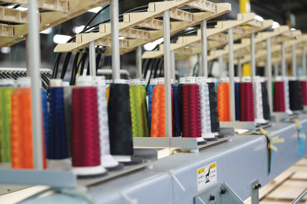 Thread in various colors arranged on a production line, with an industrial setting in soft focus.