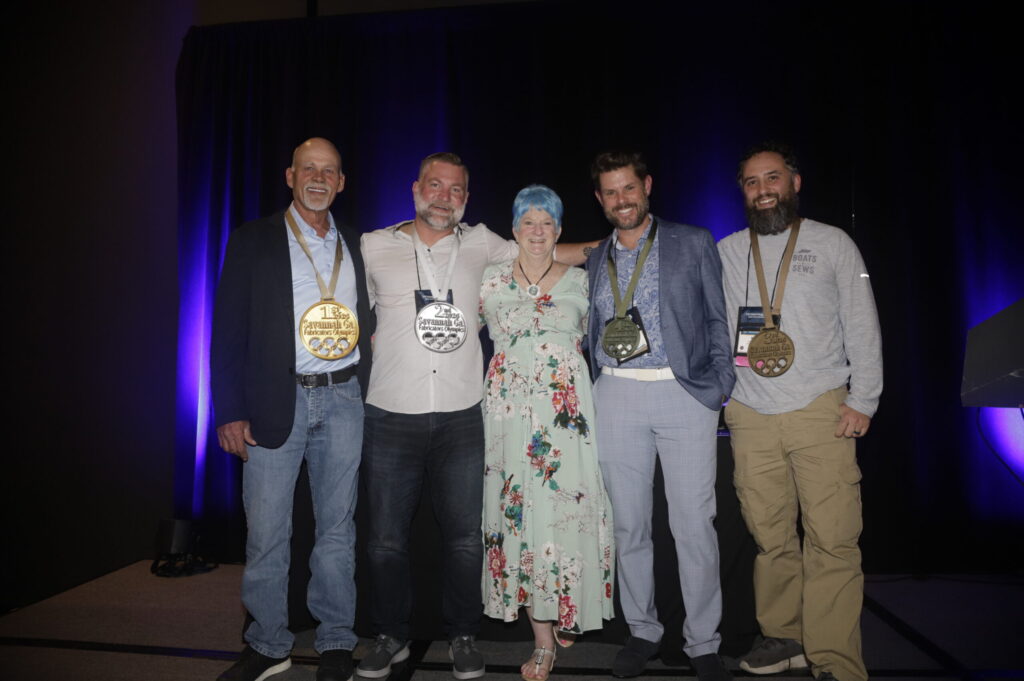 Five individuals stand together, displaying medals; they are smiling against a dark backdrop with purple lighting.