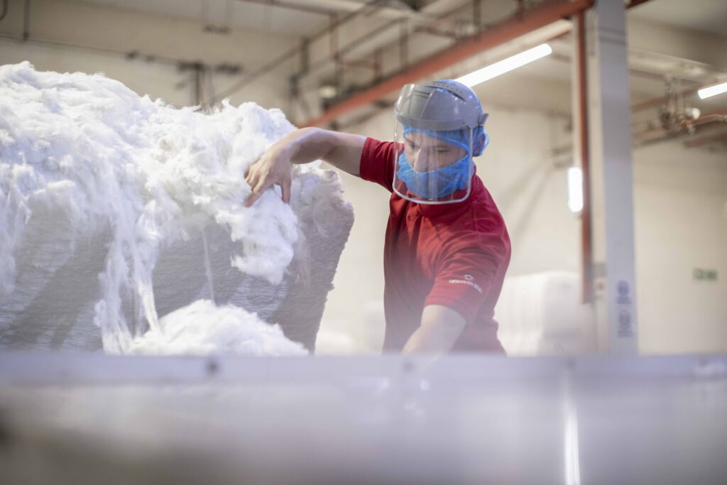 A worker in a red shirt and blue hairnet handles fluffy white material in a bright industrial setting.