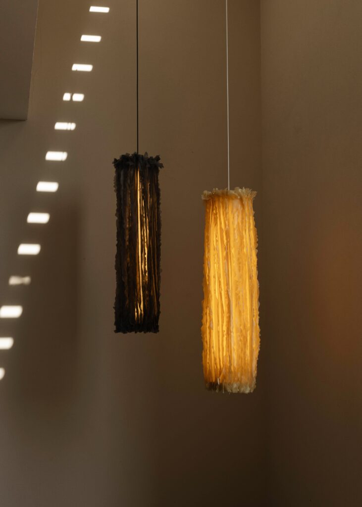 Two textured pendant lamps hang from the ceiling, one in dark grey and the other in warm yellow, casting soft shadows on the wall.