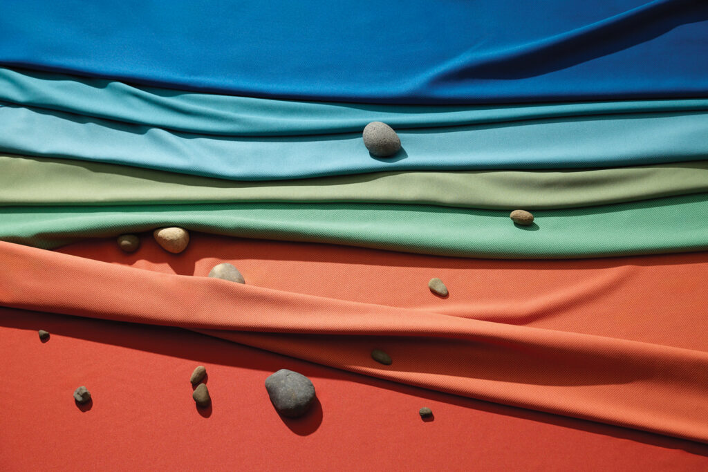 Layers of upholstery fabric in blue, teal, green and orange intertwined with smooth pebbles.