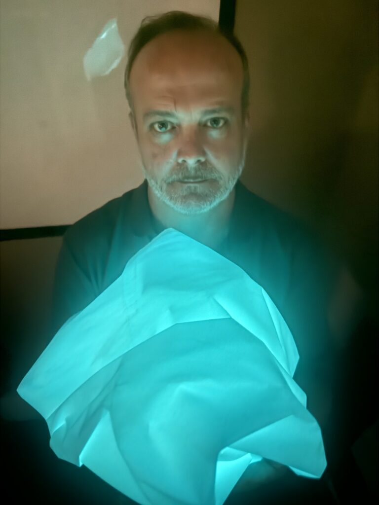 Daryl Thompson, who has a serious expression, holds a balled-up, illuminated fabric that glows light blue. It is Project Aura, a project of Global Research and Discovery Group.