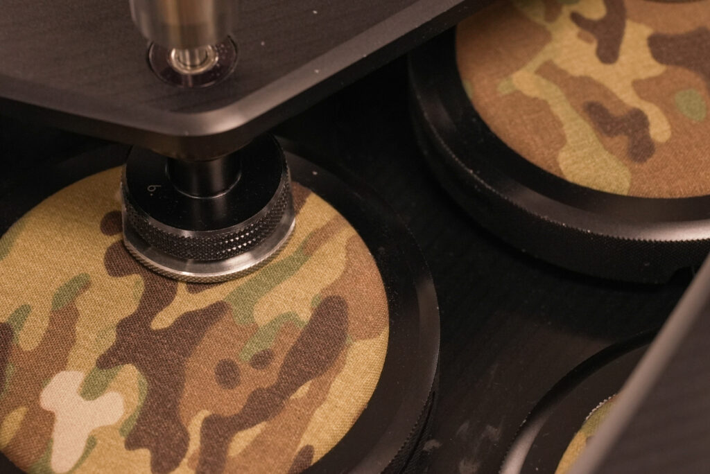 Close-up of a machine tool pressing on camouflaged fabric, featuring a textured black base and metallic components.