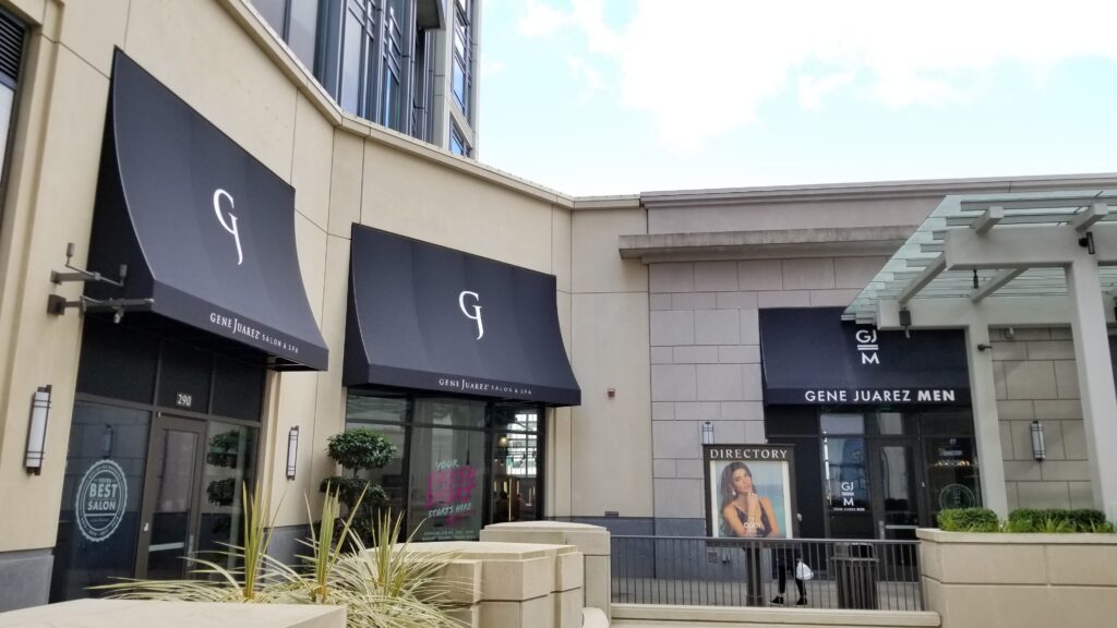 Two storefronts featuring sleek black awnings with white lettering and logos above the entrances, set against a modern architectural backdrop.