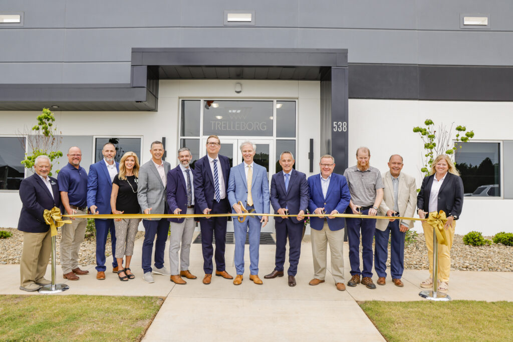 Trelleborg FC Opening 3 A group of executives and officials in business attire stand together, smiling, in front of a modern building, holding a large gold ribbon.