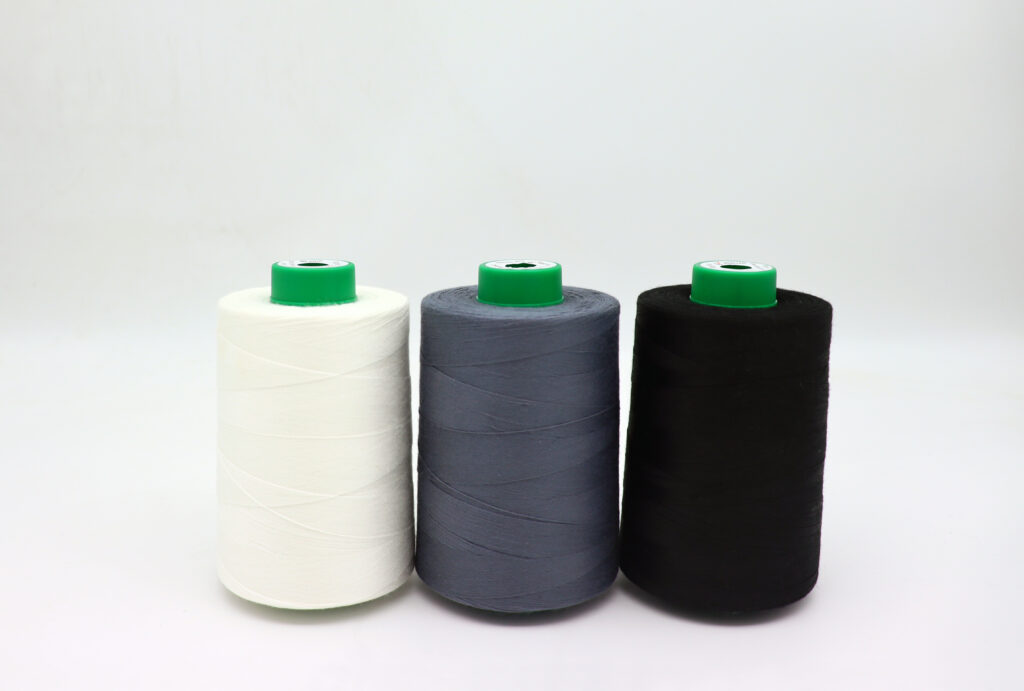 Three spools of thread in white, grey and black, each with a green cap, displayed in a row against a light background.
