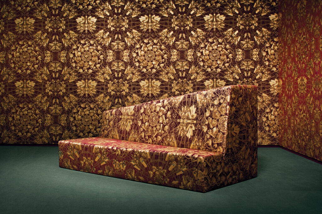 Sleek sofa covered in vibrant silk patterns sits against a richly patterned, golden-red silk tapestry of the same fabric, creating a striking visual impact. The artwork The artwork is by Ai Weiwei, The Animal That Looks Like a Llama but Is Actually an Alpaca. The setting was in the Rubelli showroom. 
