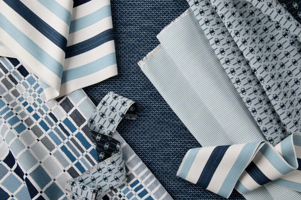 A collection of blue and white fabrics in various patterns, including stripes, checks, and textures, arranged artistically on a dark background from Sunbrella's CW Collection.