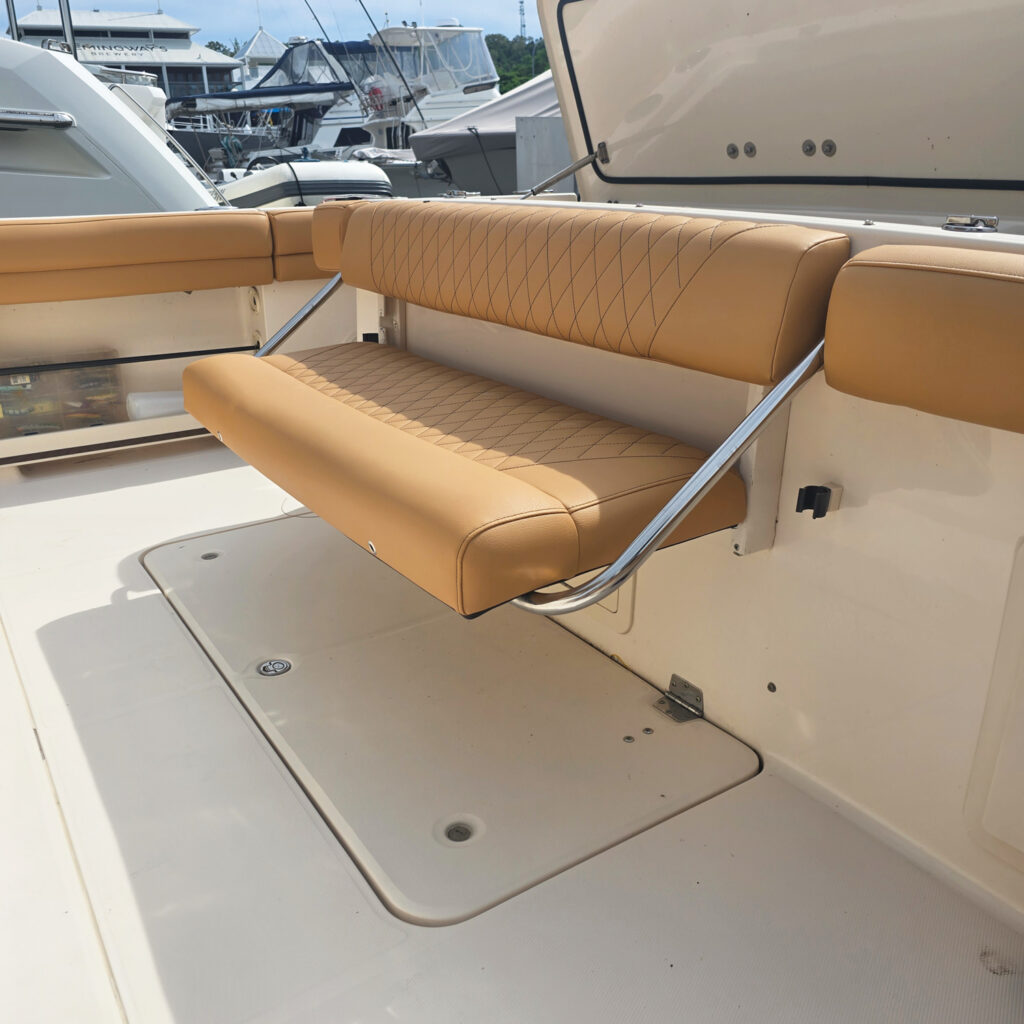 A tan cushioned bench with diamond stitching, mounted on a boat's deck, overlooks a marina filled with boats.