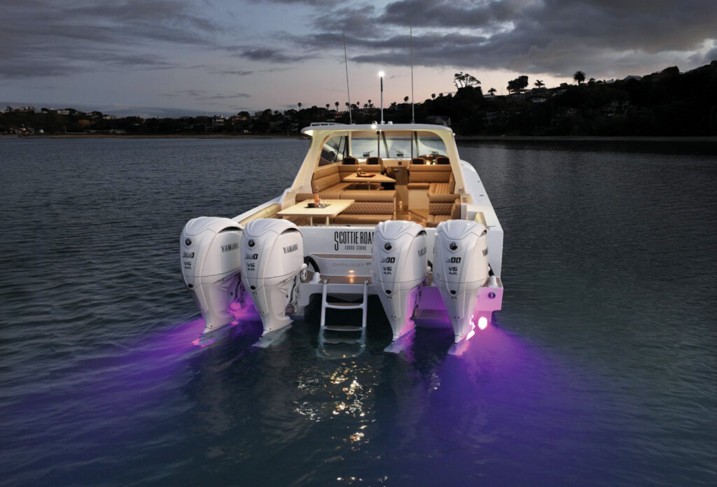 A sleek boat with three outboard motors illuminated in purple light, docked on calm water at twilight.