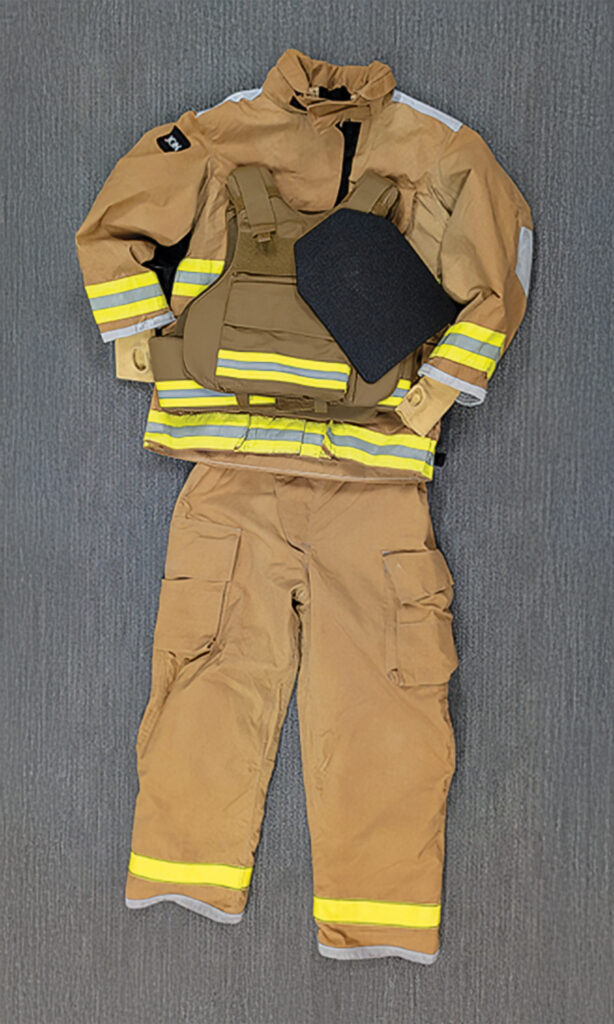 Tan firefighter turnout suit laid flat, featuring reflective yellow stripes, a tactical vest, and a protective panel, on a textured gray background.