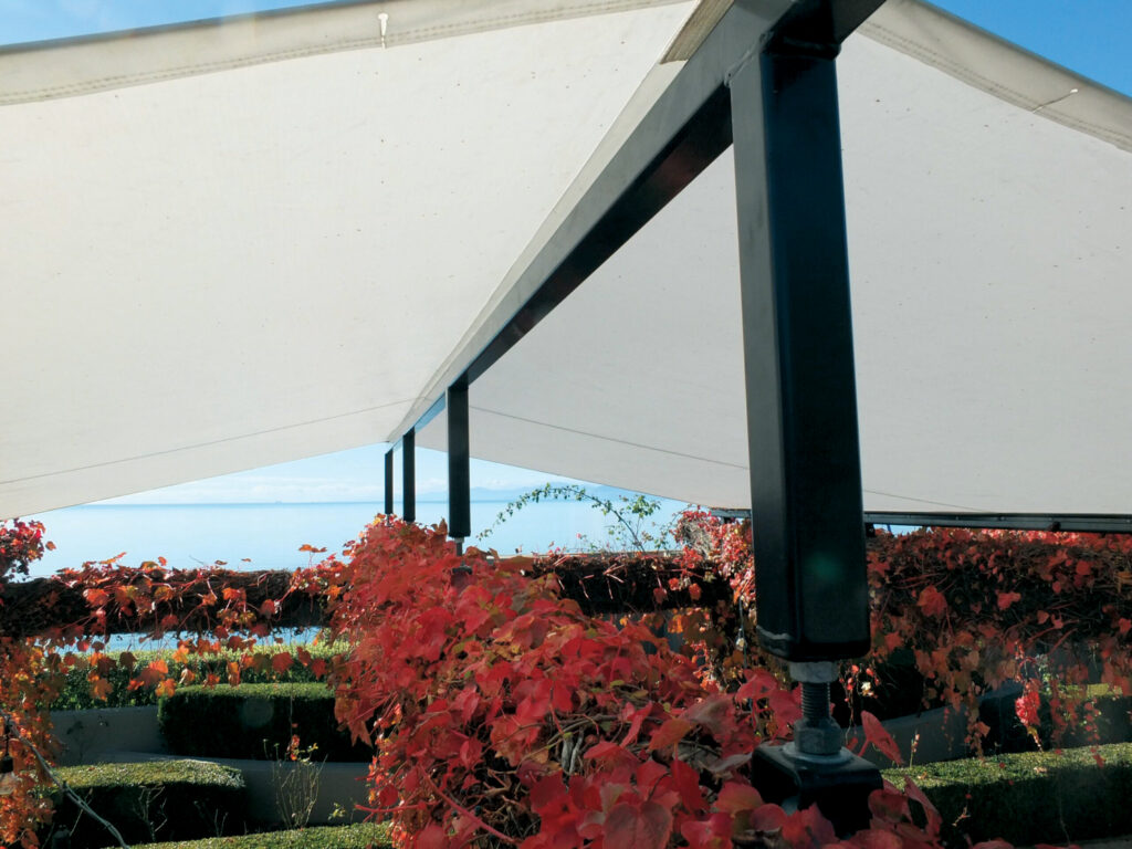 White canopies stretch above red foliage, framed by dark structural supports, with a view of the sky in the background.