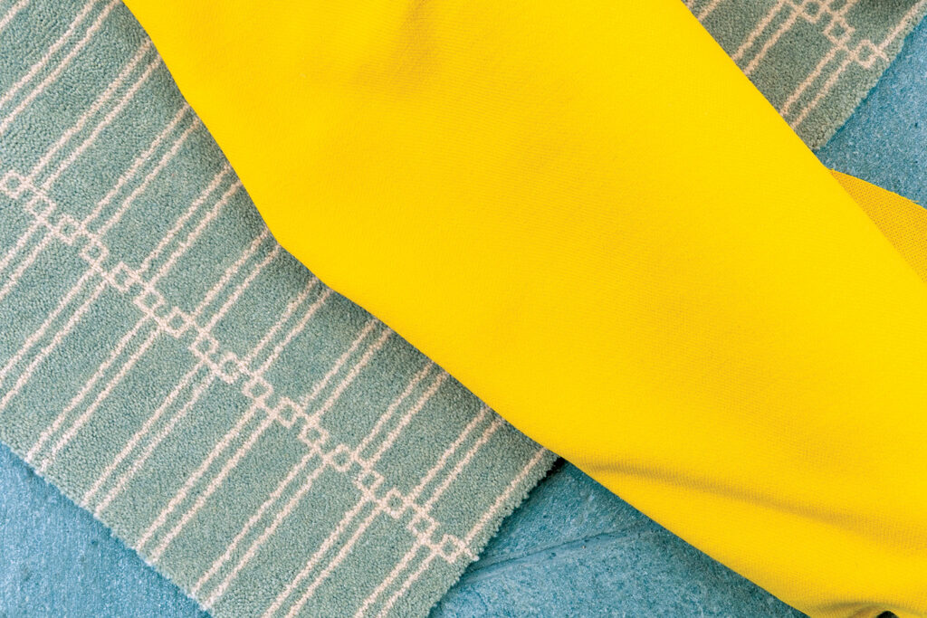 Close-up of silk textile featuring a vibrant yellow section overlaying a textured, soft green fabric with subtle stripes.