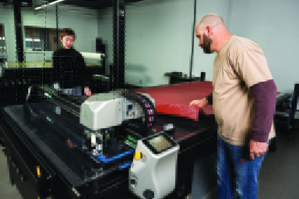 Greg Thompson and Tianna Lind operate an Autometrix cutting machine in a well-lit facility, with red material being cut.