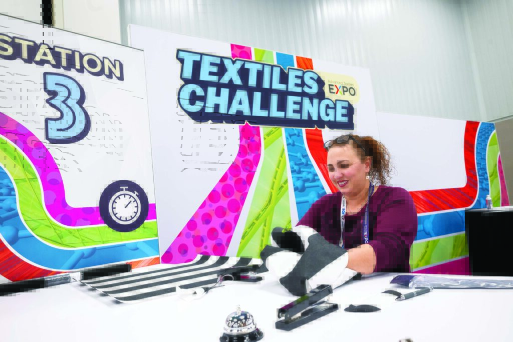 A woman participates in a textiles challenge at a booth at Advanced Textiles Expo, with colorful backdrop elements and the text "Station 3" visible.