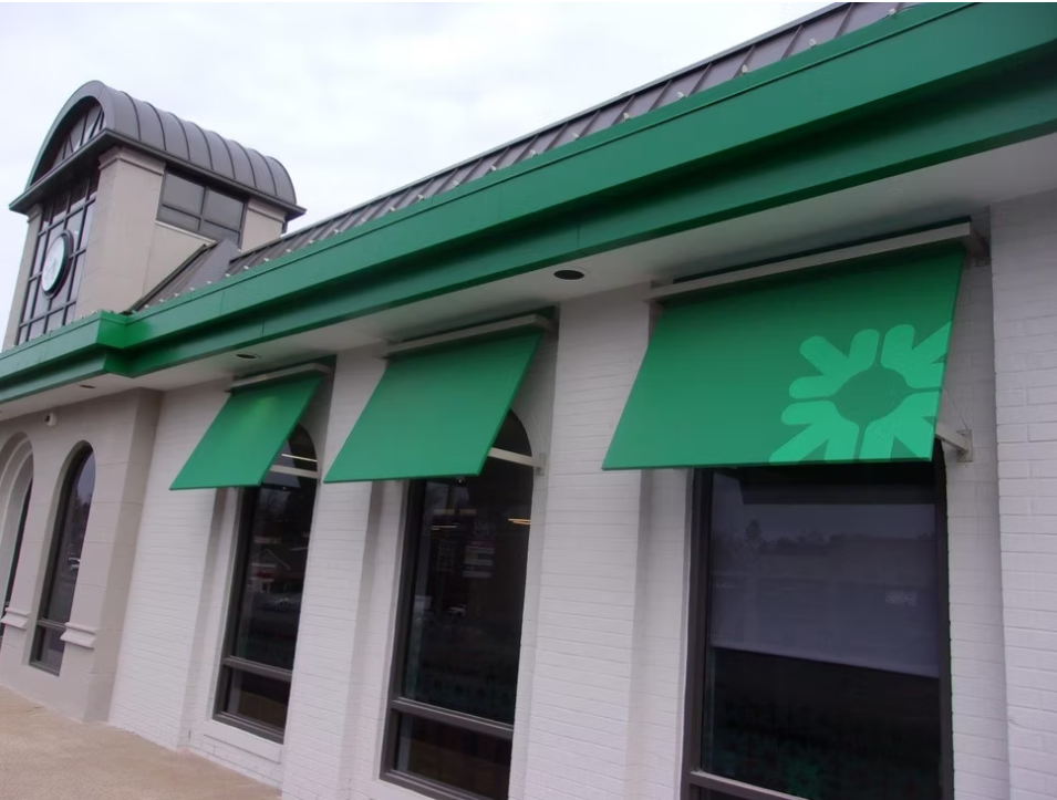Green fabric awnings with a flower pattern on a light-colored building, featuring large windows and a decorative roof element.