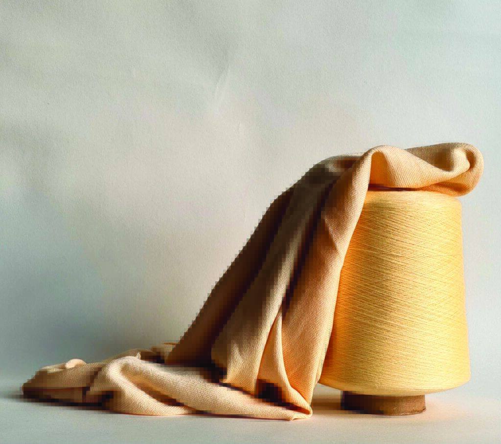 A light orange spool of thread sits beside a draped piece of soft fabric, set against a neutral background.