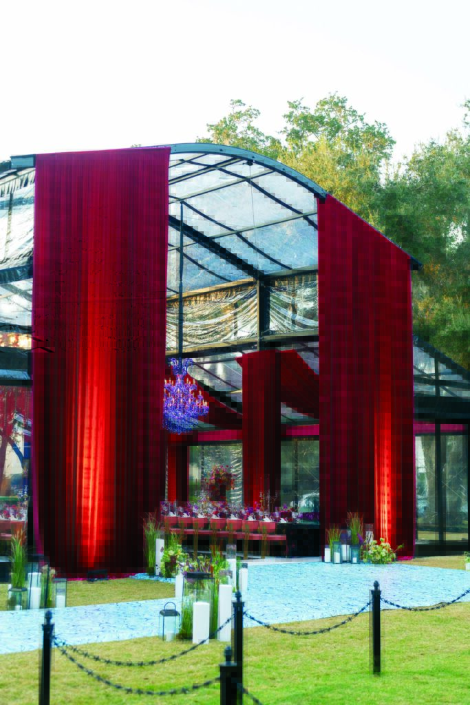 A modern wedding venue, the Horizon Garden Tent from Fred's Tents, with a glass structure, featuring red drapes, elegant tables set for dining, and a blue stone pathway.
