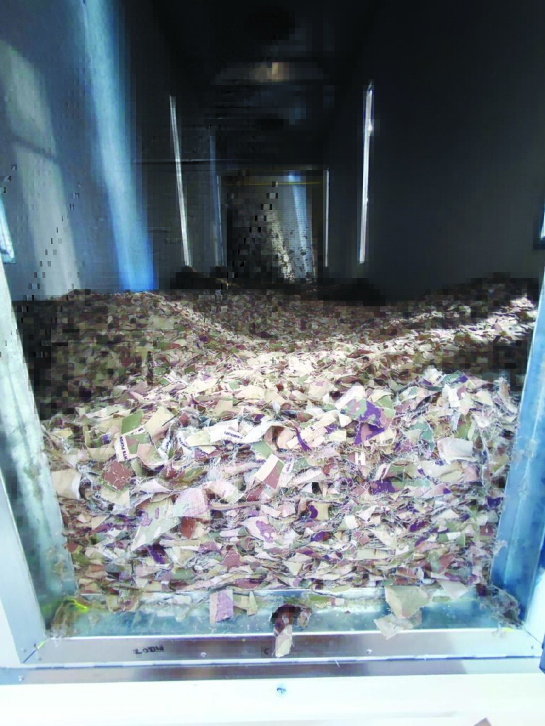 A large metal container filled with piles of colorful shredded aramid material, illuminated by natural light from two side windows.