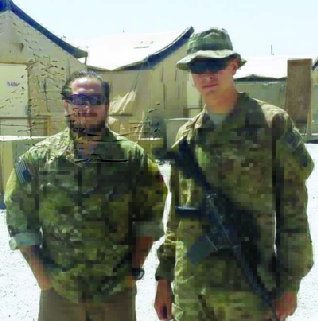 Two soldiers in military fatigues, Adam Holroyd and Zane Vogel, who started Spiritus Systems after they left the service, stand outside tents. Zane is wearing sunglasses and has an automatic firearm across his chest.