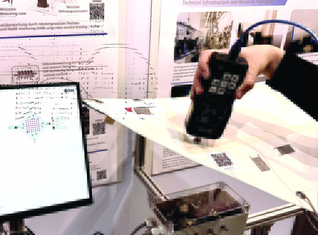 A hand holds a device measuring data on a flexible smart textile, alongside a screen displaying a graphical layout and data readings.