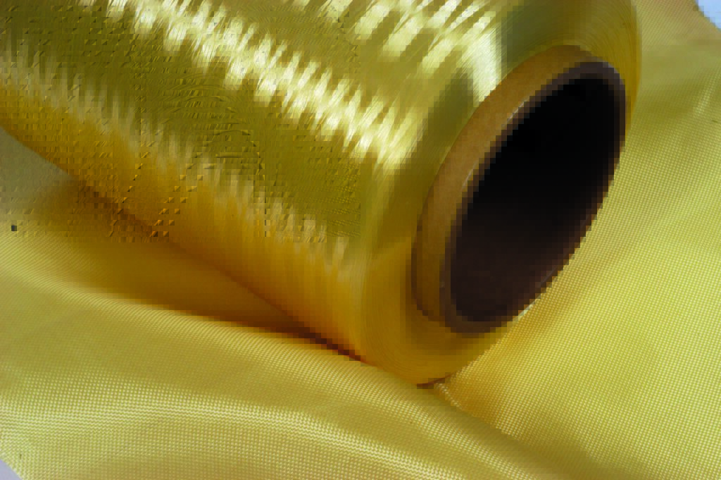 A spool of shiny yellow Kevlar fabric rests on a yellow surface of Kevlar fabric.