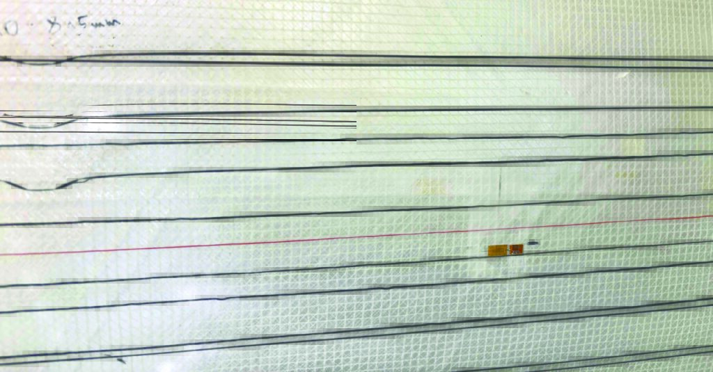 Close-up of a white textured surface with thin black lines, featuring a small yellow and black component placed along one line.