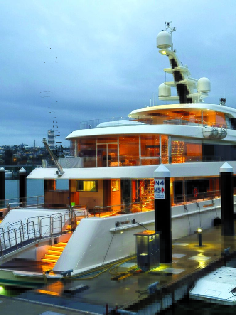 Luxury yacht docked at twilight, featuring illuminated decks and modern design, with calm water and cloudy sky in the background.