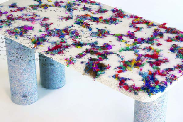 A textured table featuring a colorful surface with vibrant fabric scraps, supported by cylindrical pillars in a light color.