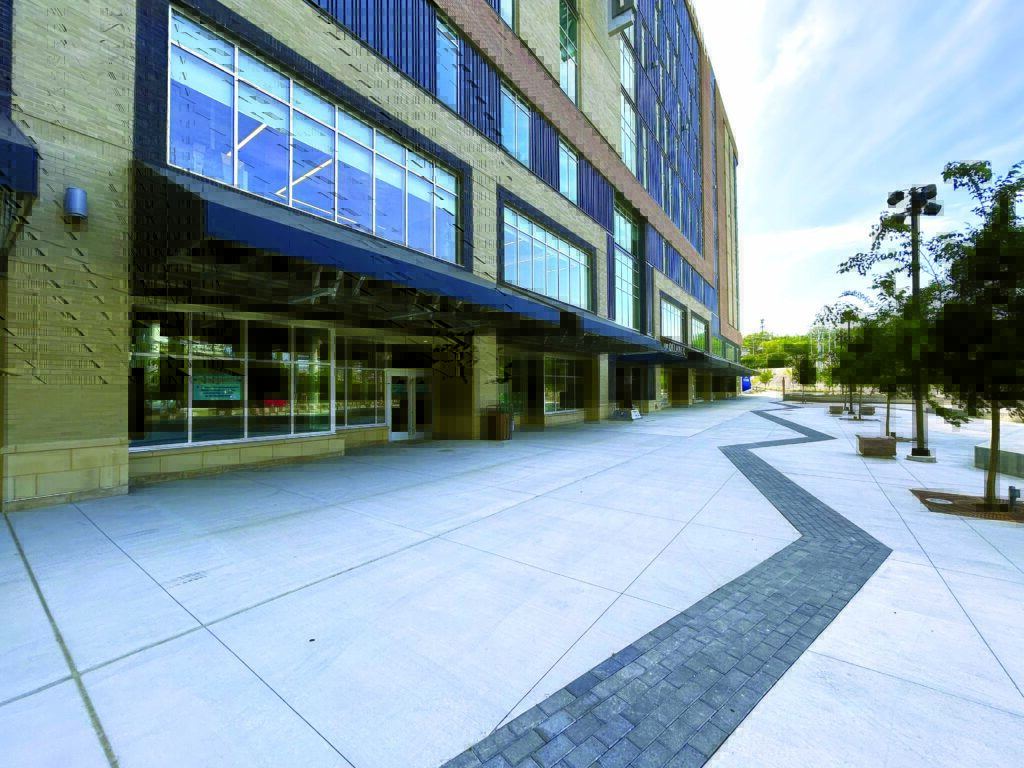 Modern building facade of the Beauford Delaney Building in Knoxville, Tenn., with large windows and awning overhangs. There is a wide, patterned sidewalk and trees lining the space.