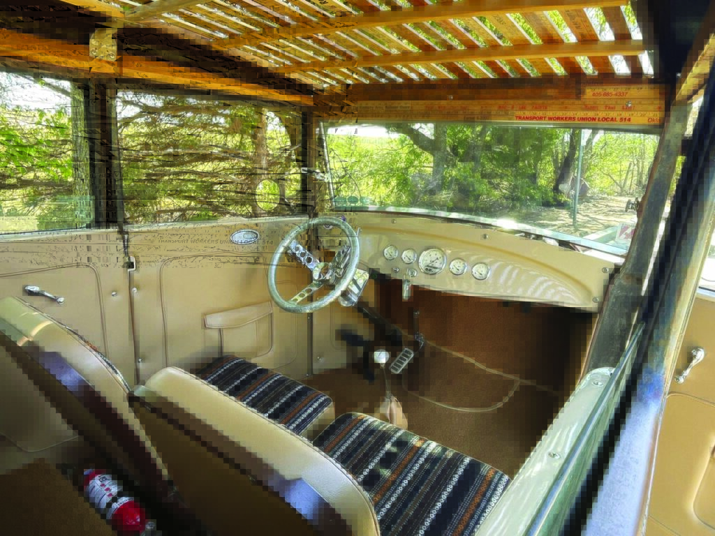 Interior of a vintage Model A car featuring a wooden headliner, striped seats, classic steering wheel, and dashboard with round gauges.