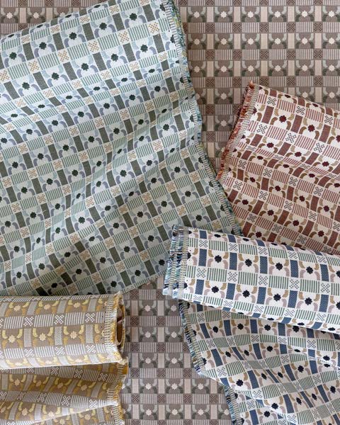 Textiles featuring intricate patterns in soft colors, including green, rust, and mustard, arranged against a checkered background.