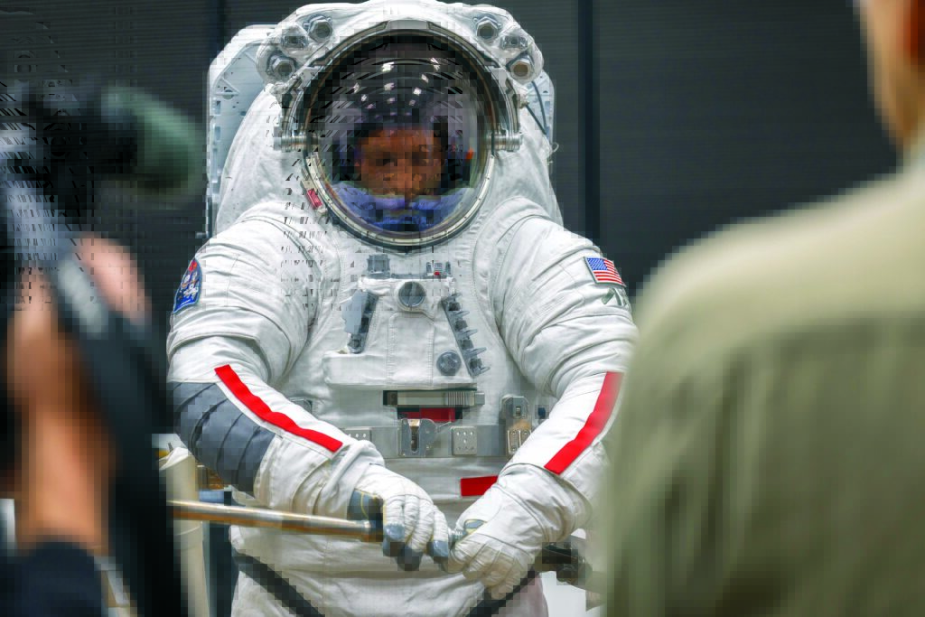 An Axiom Space engineer wearing the Axiom Extravehicular Unit suit prepares tools, focused intently, in a professional setting.